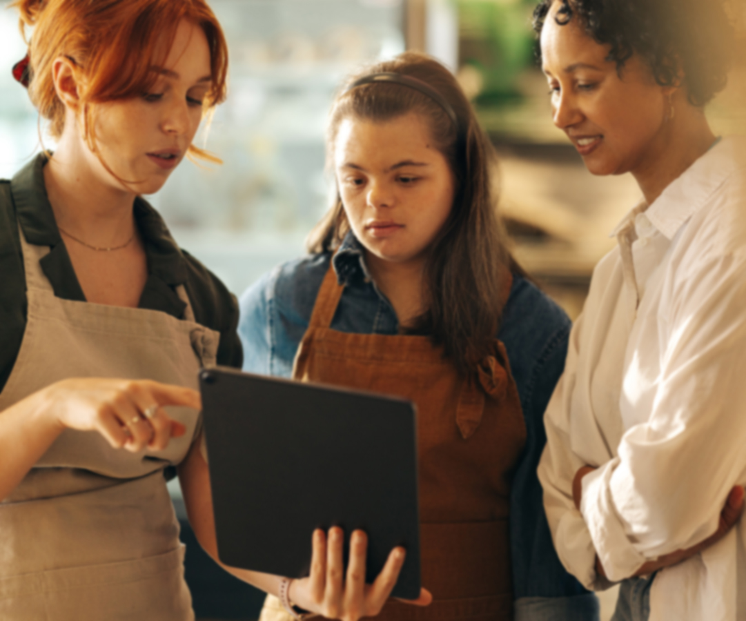 Supermarket manager using a digital tablet while having a discussion with her employees in a staff meeting. Group of diverse women working together in an all-female small business.